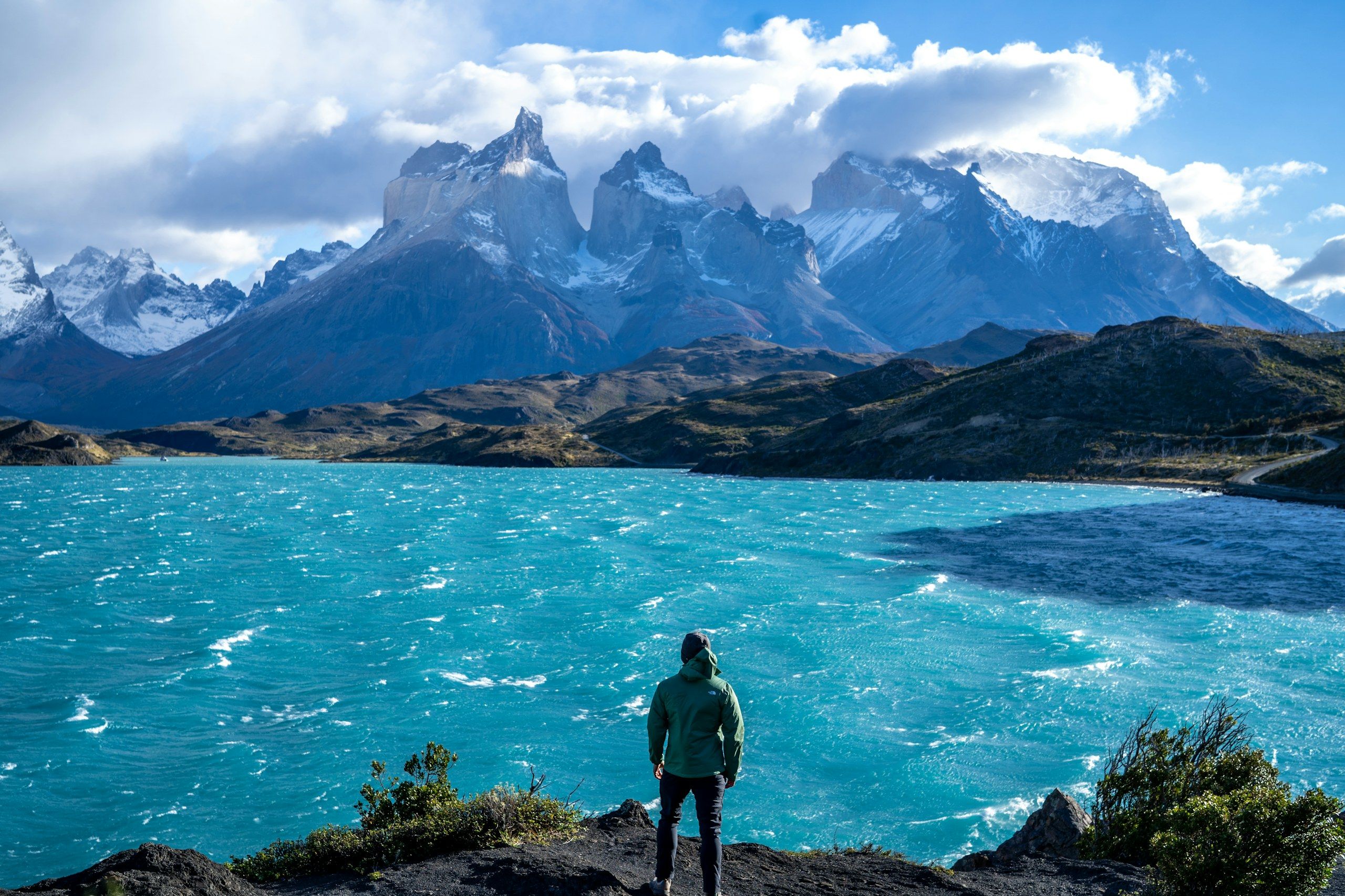 A person facing a turquoise lake and the mountains of Torres del Paine, Chile.