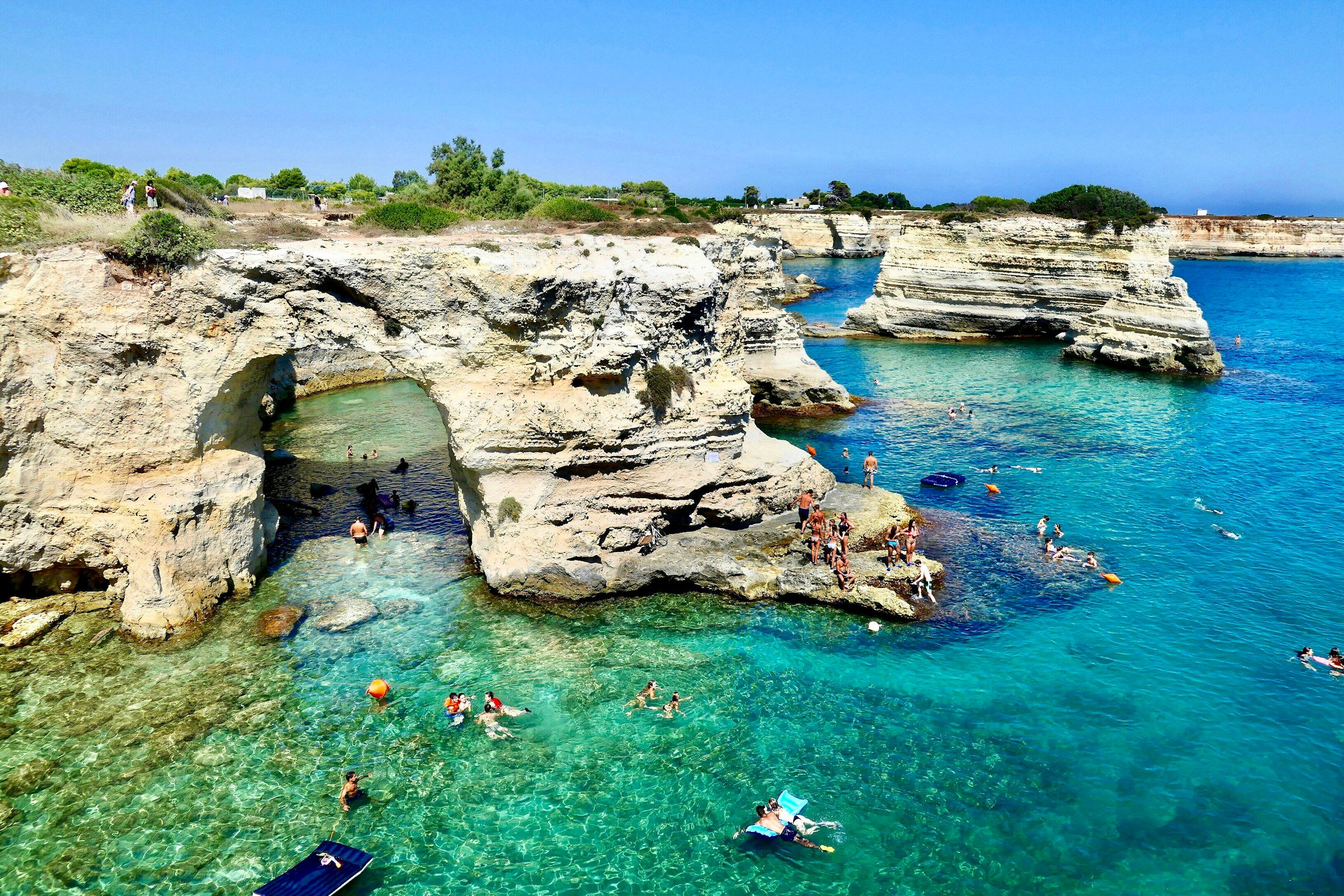 The cliffs of Torre Sant’Andrea in the Salento, with turquoise sea and people swimming.