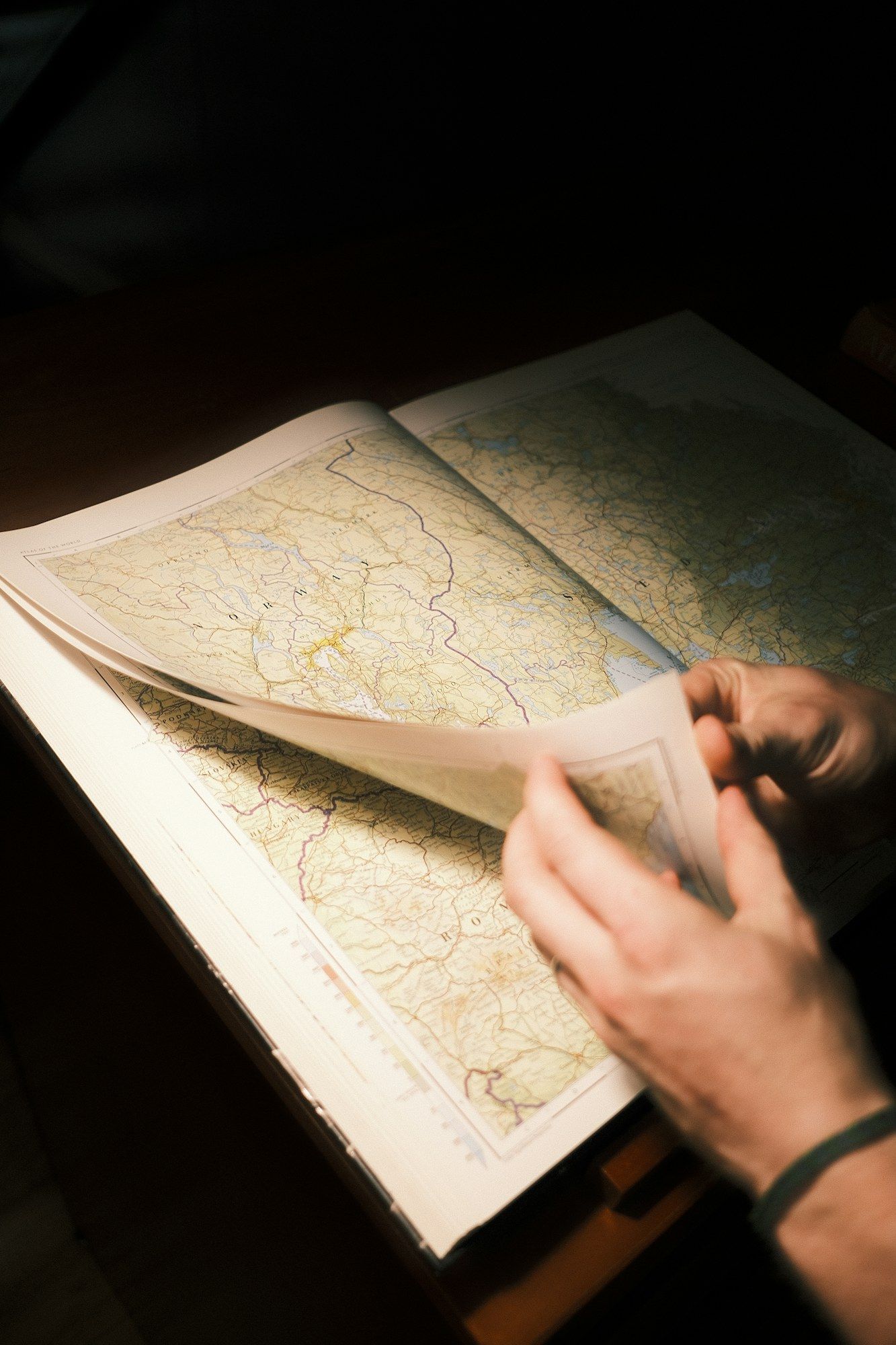 Hands opening a paper map on a table in warm light.
